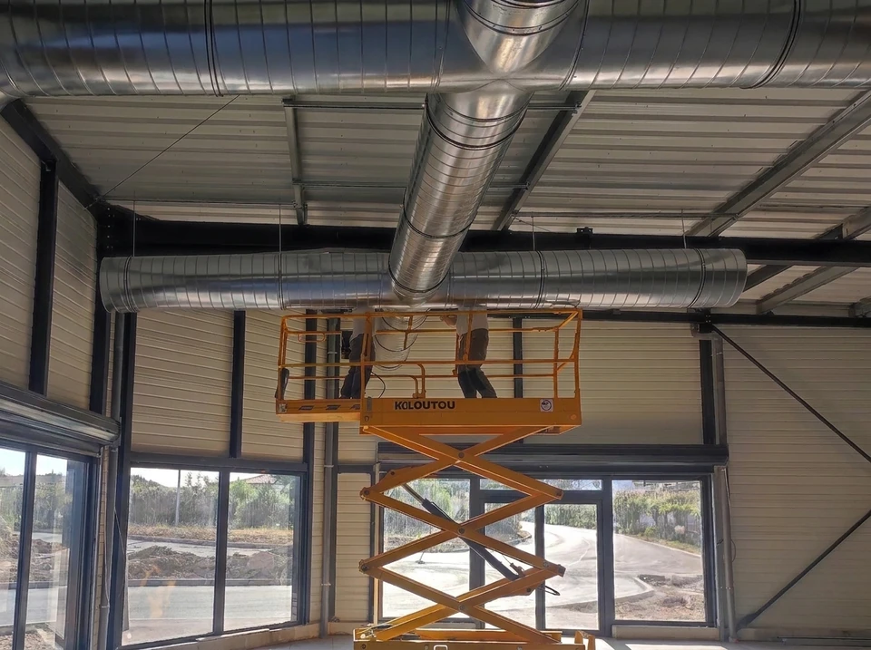 Technicien en tenue de travail grise allongé sur un rebord extérieur en hauteur, accédant via une échelle coulissante aluminium à double section